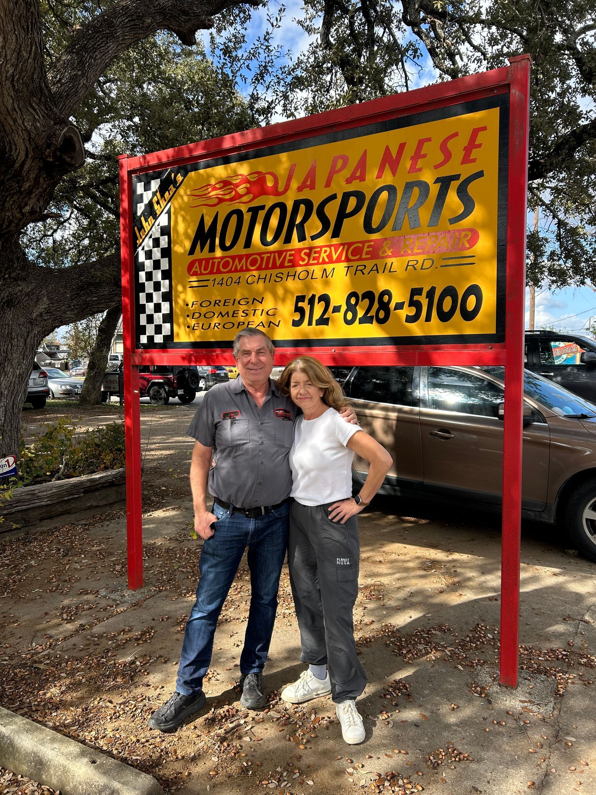 A man and a woman are standing in front of a sign for Japanese Motorsports