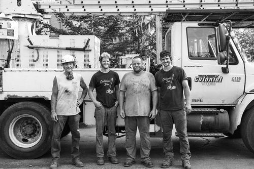 Four workers stand in front of a white utility truck in an industrial yard.