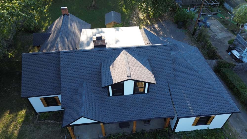 Aerial view of a white house with a dark gray roof, dormer, and chimney. Sunlight highlights the structure.
