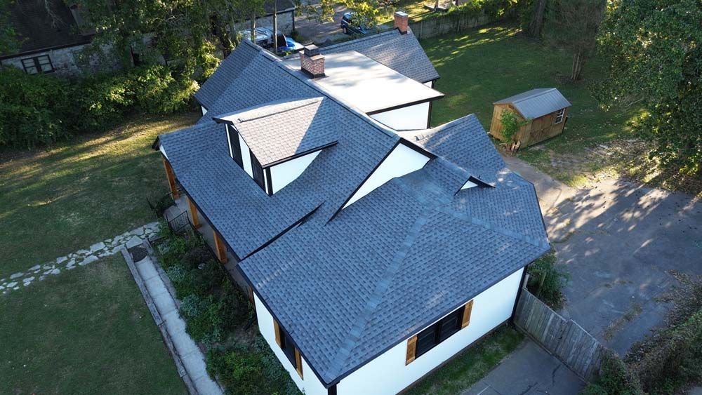 Aerial view of a white house with a dark gray roof, surrounded by green grass and trees.