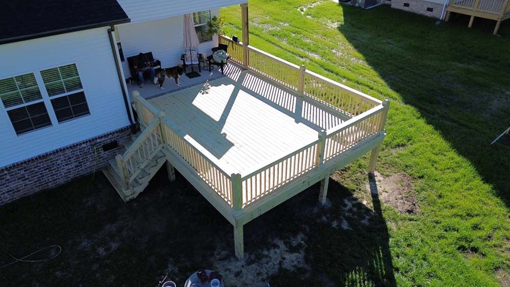Wooden deck attached to a house with stairs, railing, and a covered section; set on green grass.