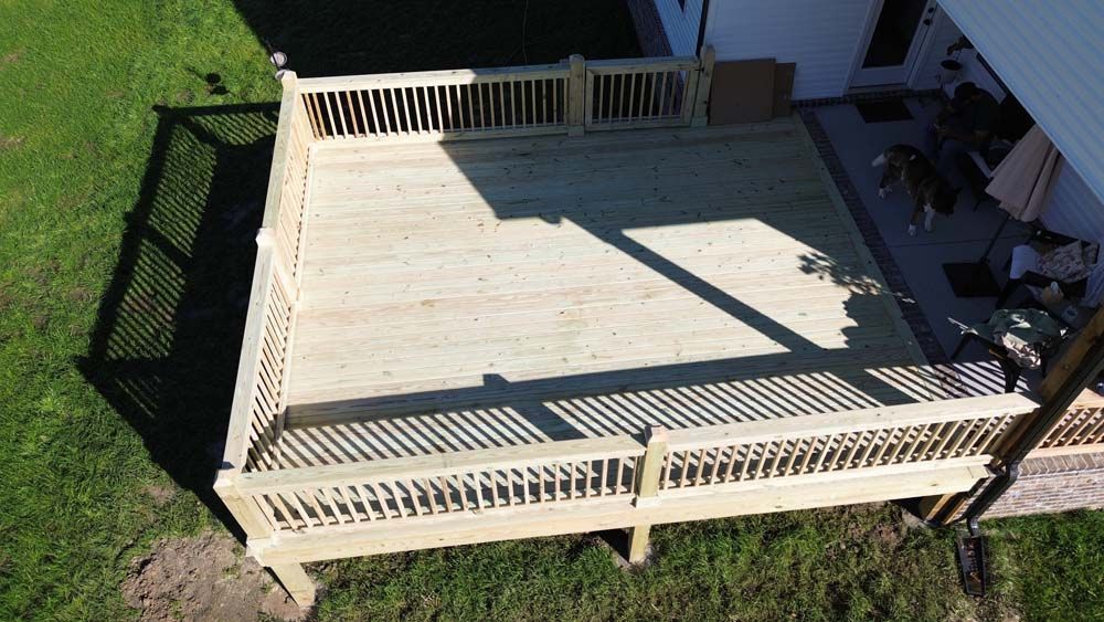 Wooden deck with railing, connected to a house. Shadows cast on grass from the deck.