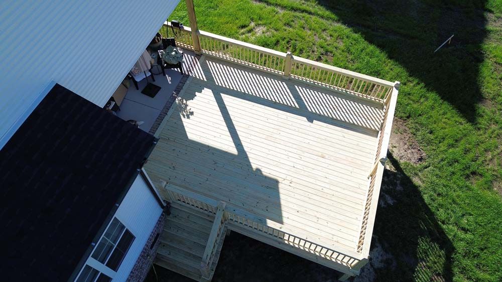Overhead view of a wooden deck attached to a house with a railing, overlooking a grassy yard.