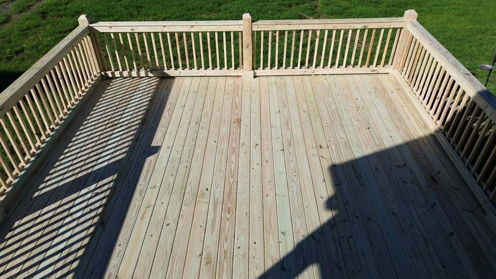 Wooden deck with railing, casting shadows on the surface, on a sunny day.