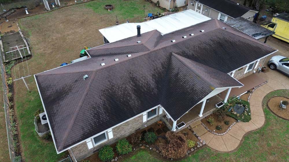 Overhead view of a house with a brown roof and white trim, surrounded by grass and a paved pathway.