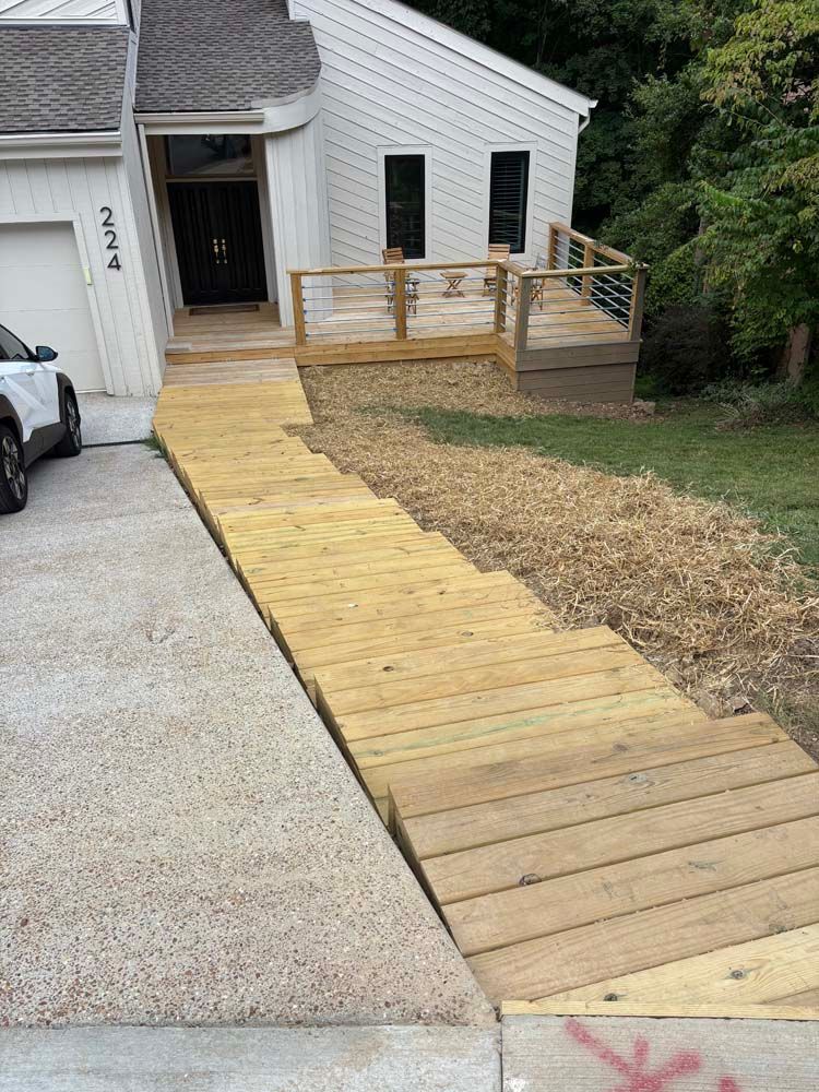 Wooden ramp and steps leading to a house entrance. House has a deck and garage.