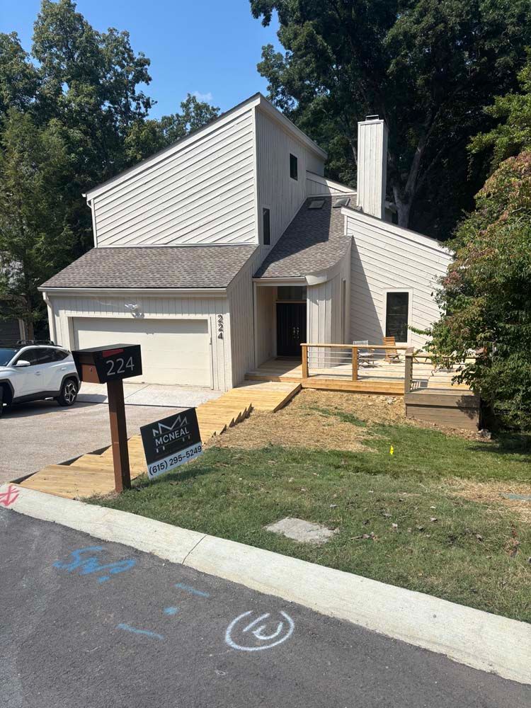 Beige two-story house with a wooden deck, driveway, and mailbox in front.