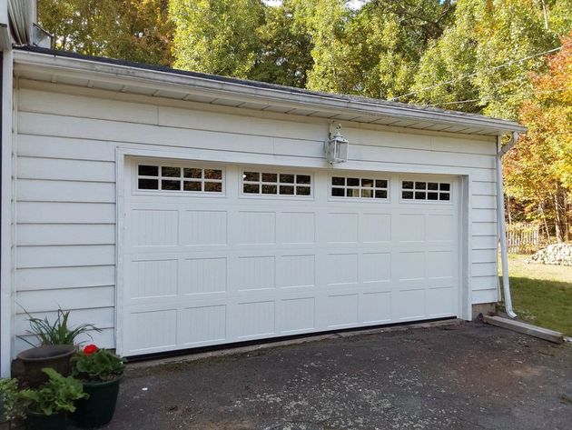 White garage door with small windows on a driveway beside a house, surrounded by trees in fall.