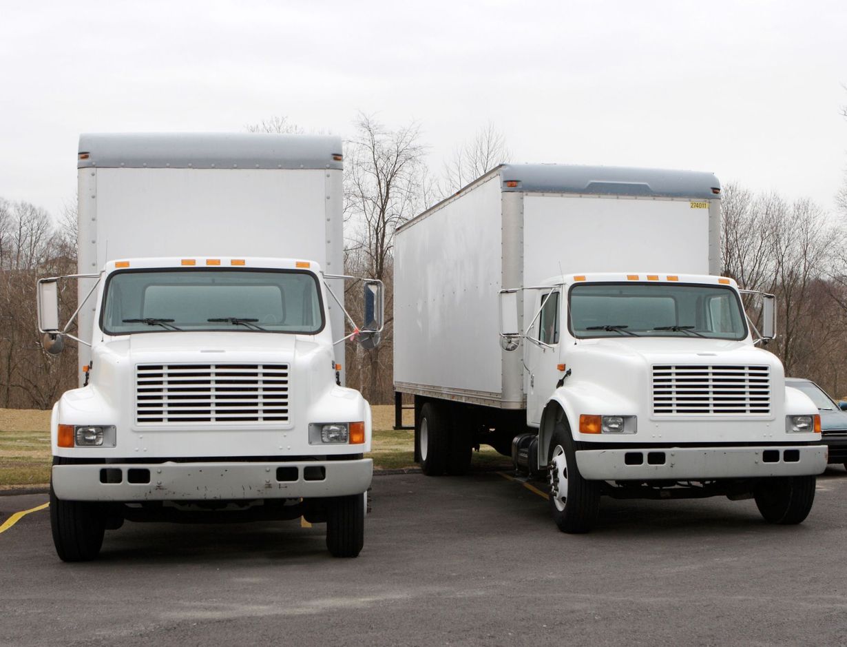 Two white box trucks parked side by side in a lot