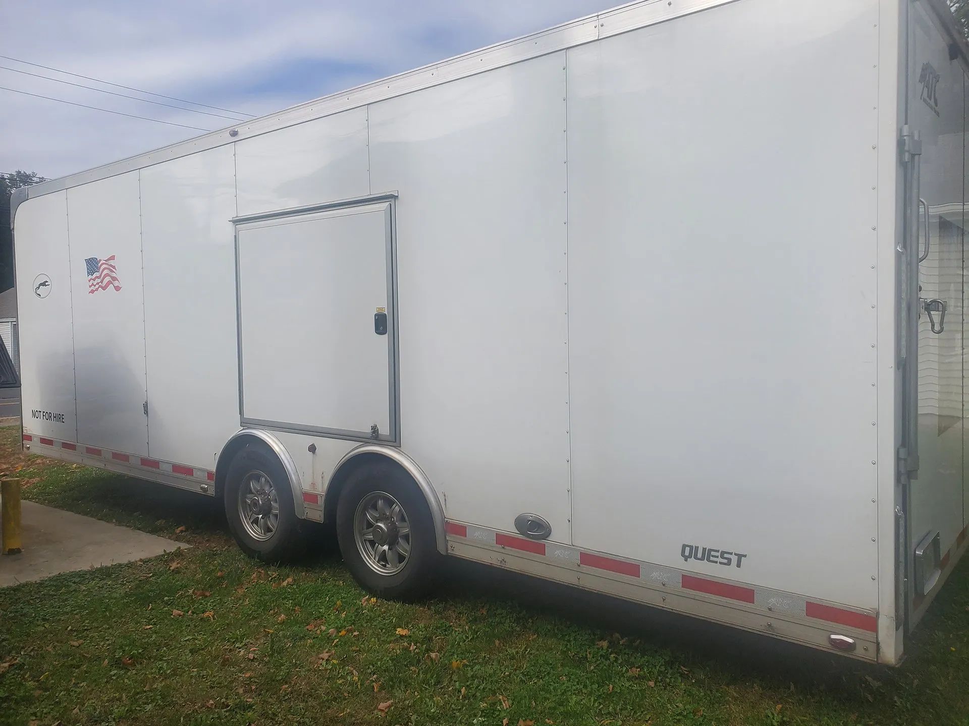 White enclosed cargo trailer with dual axles parked on grass under cloudy sky