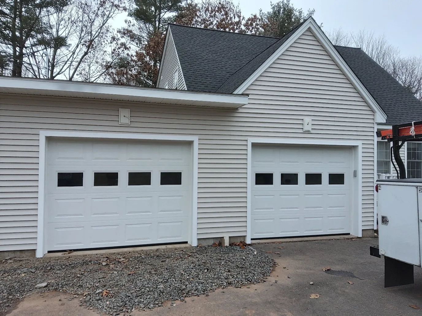 Two white garage doors on a house with gray siding and a gravel driveway