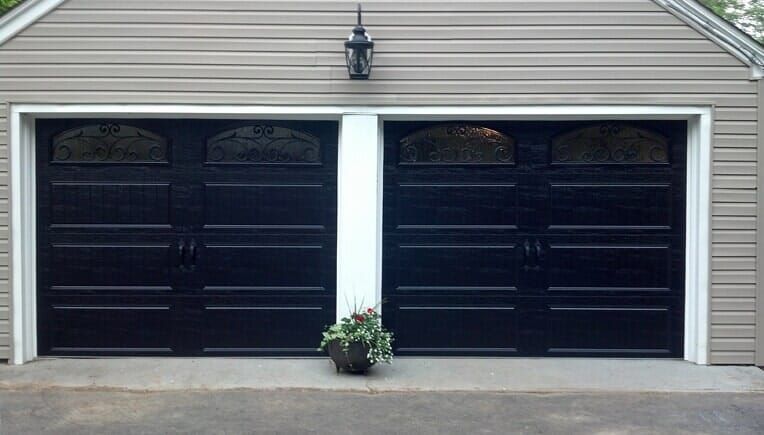 Two black garage doors on a beige house, with a small potted plant centered between them.