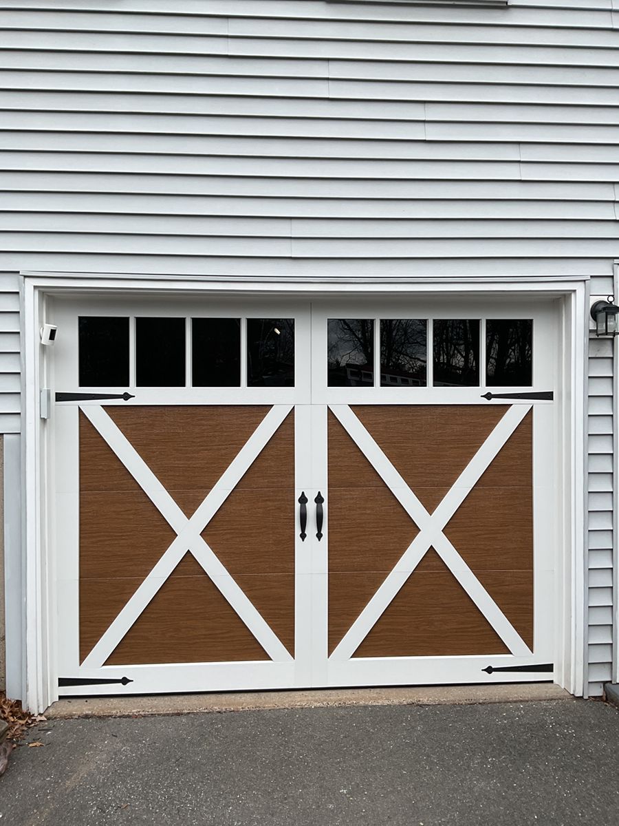White double garage doors with brown X-bracing and small windows on a gray-sided house.