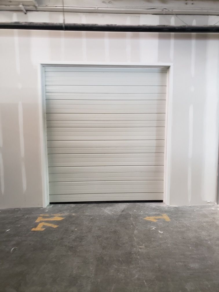 Closed white roll-up door in a warehouse interior with a concrete floor.