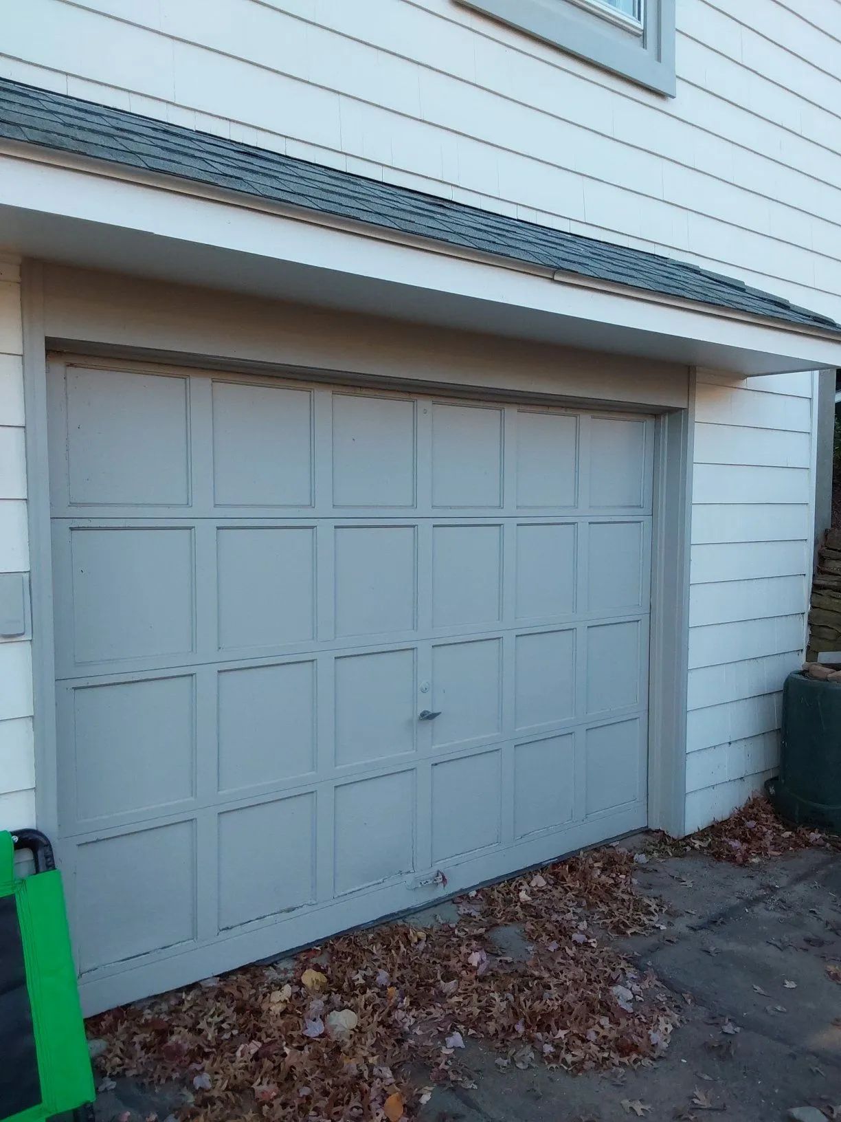 Gray garage door on a house exterior with leaves scattered on the driveway