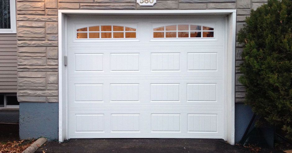White garage door with small arched windows on a stone house exterior