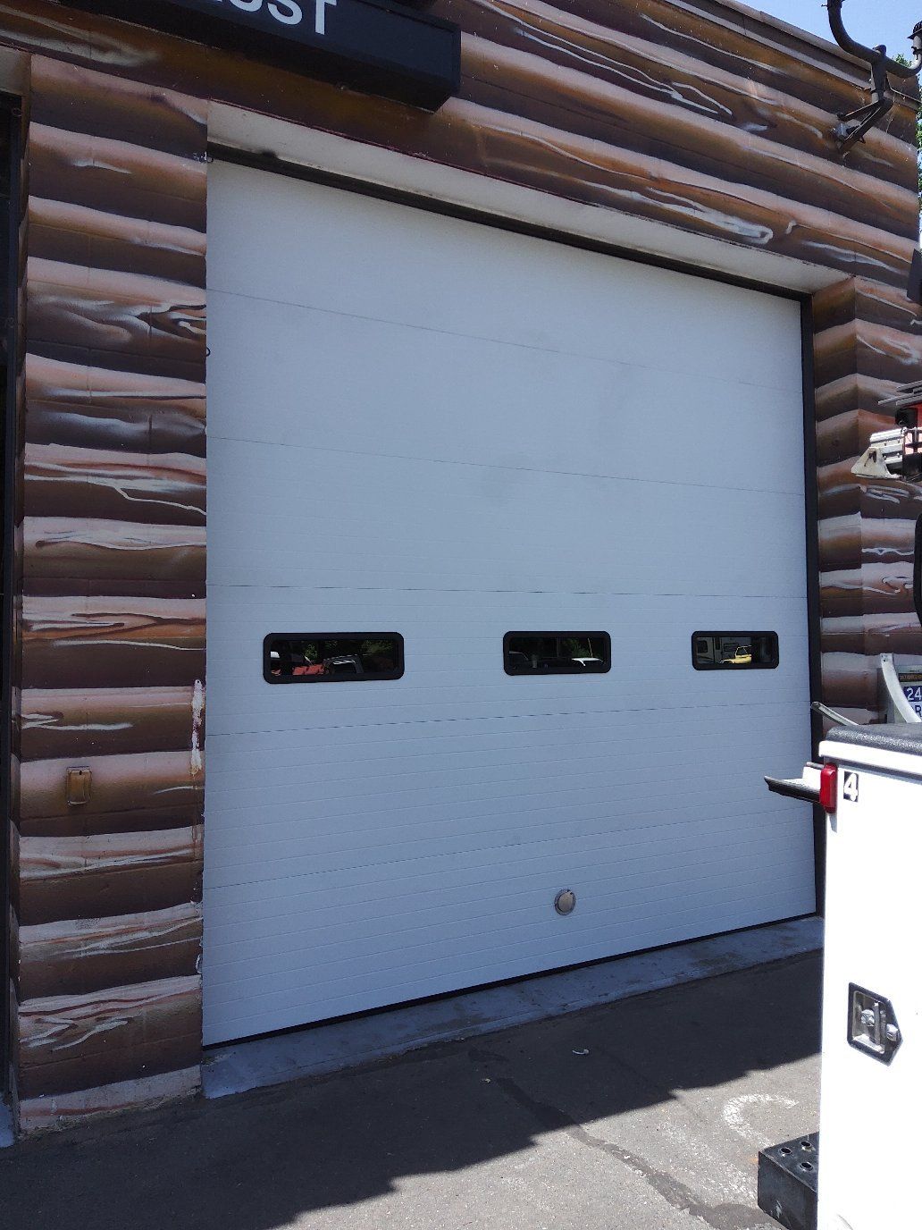 White garage door with three small windows set in a log cabin wall, viewed from outside.