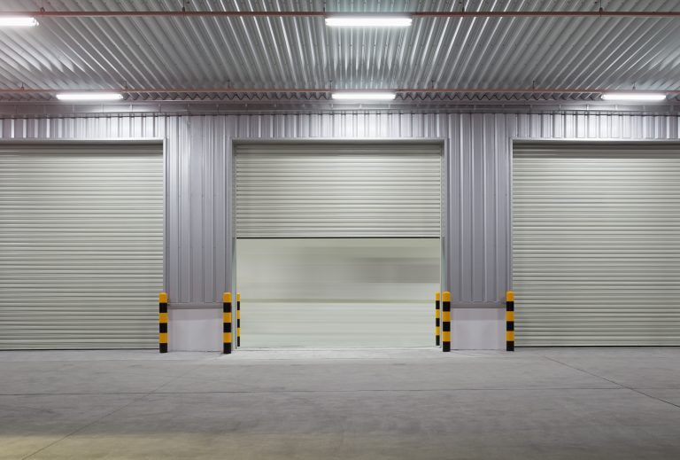 Empty warehouse interior with three gray roll-up doors and black-yellow safety bollards