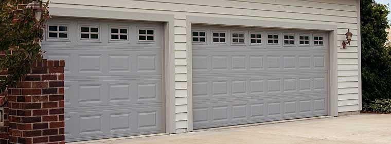 Two gray garage doors on a beige house with brick trim and a small wall lantern