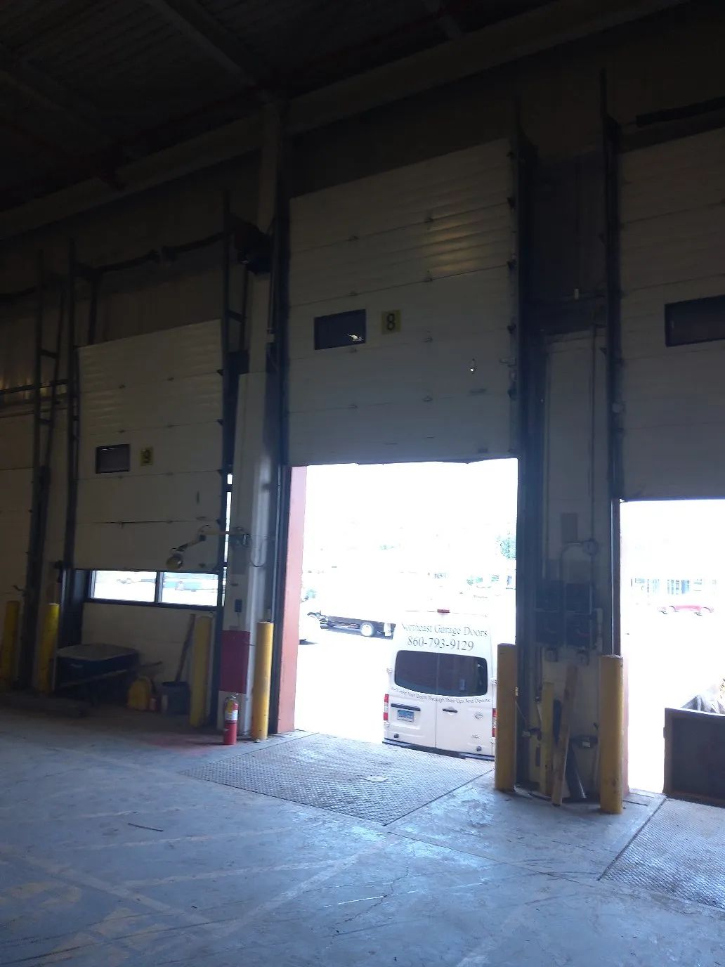 Warehouse loading dock with two open garage doors and bright daylight outside
