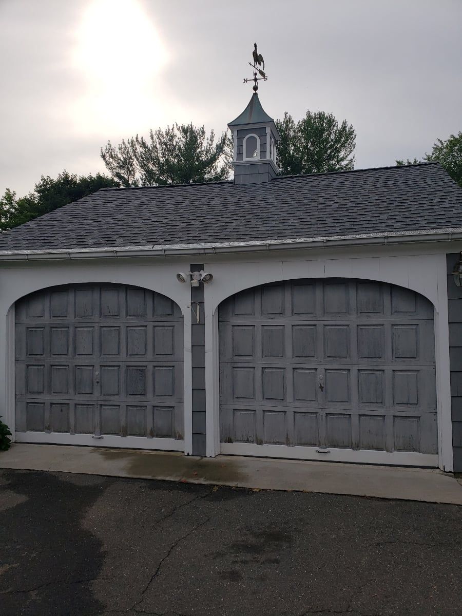 White double garage with gray doors under a cloudy sky, with a cupola visible behind the roof.