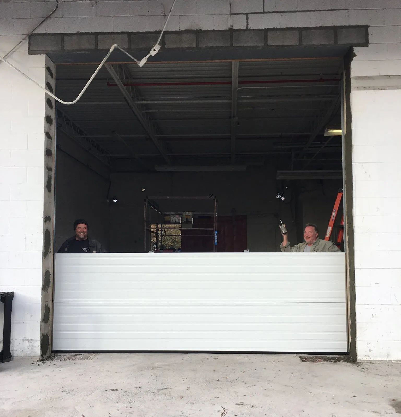 Two people behind a partially closed white garage door in a warehouse opening