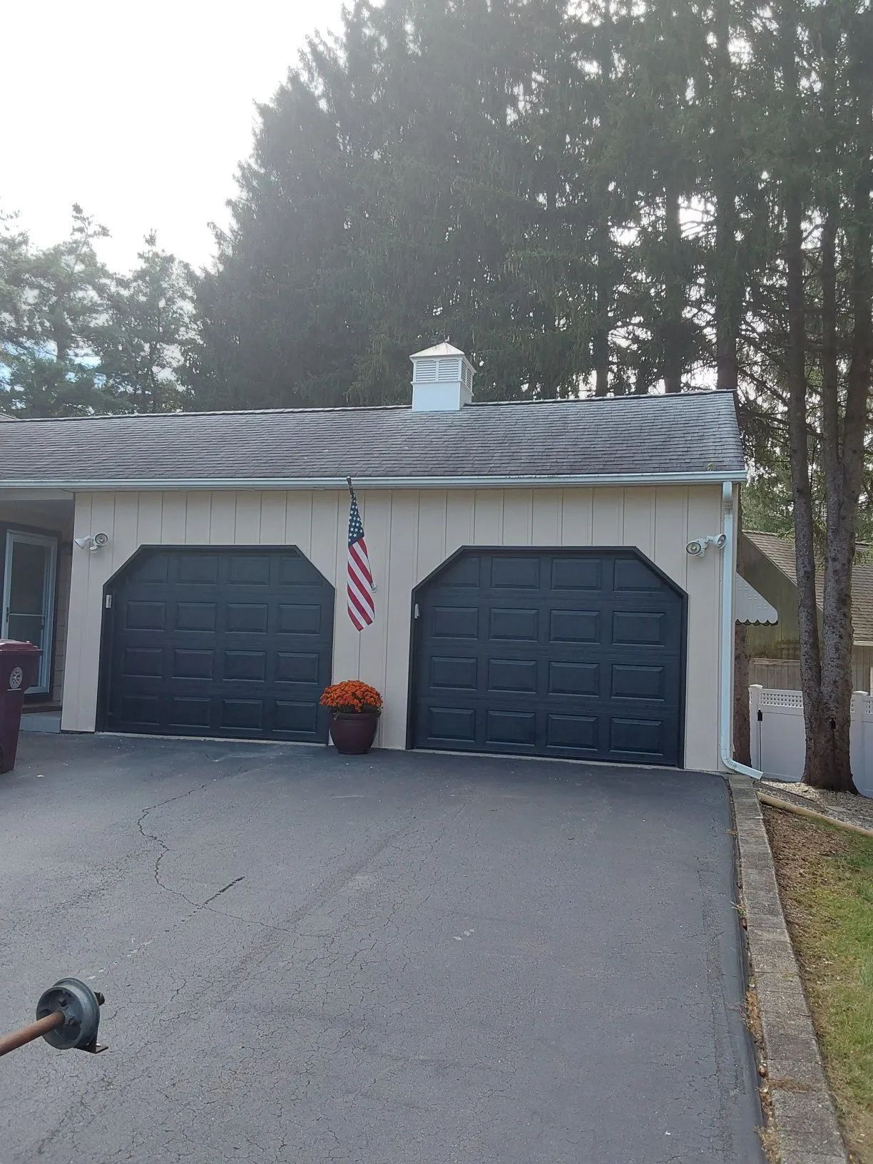 Two-car garage with dark blue doors, American flag, and flower pot in front of a beige house