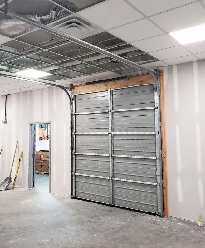 Interior under renovation with a large metal garage-style door and exposed ceiling panels
