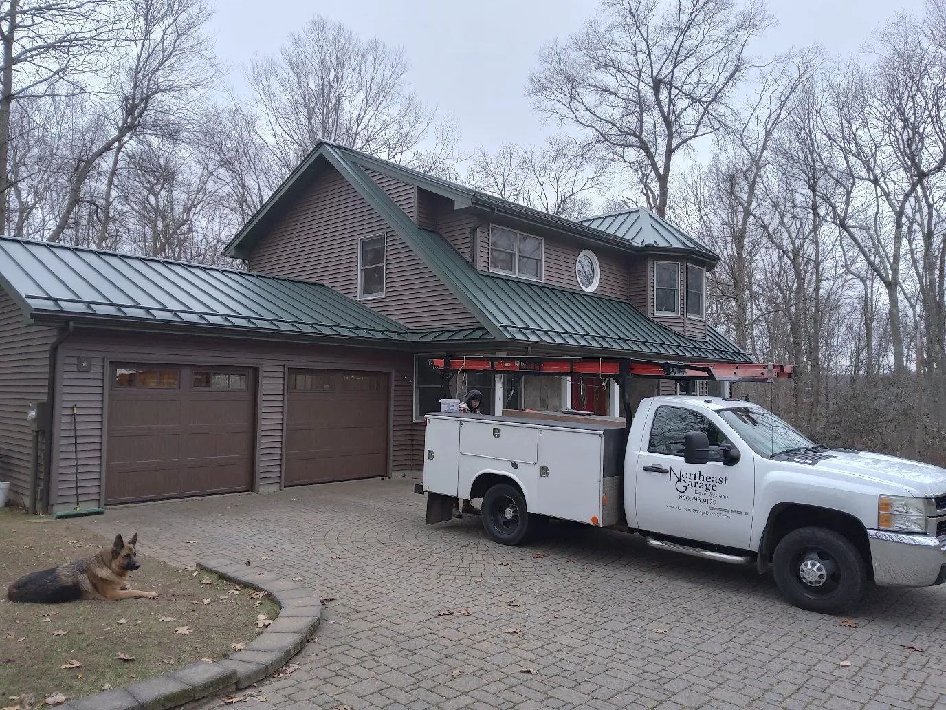 White utility truck parked outside a rustic house with garage, under a gray sky.