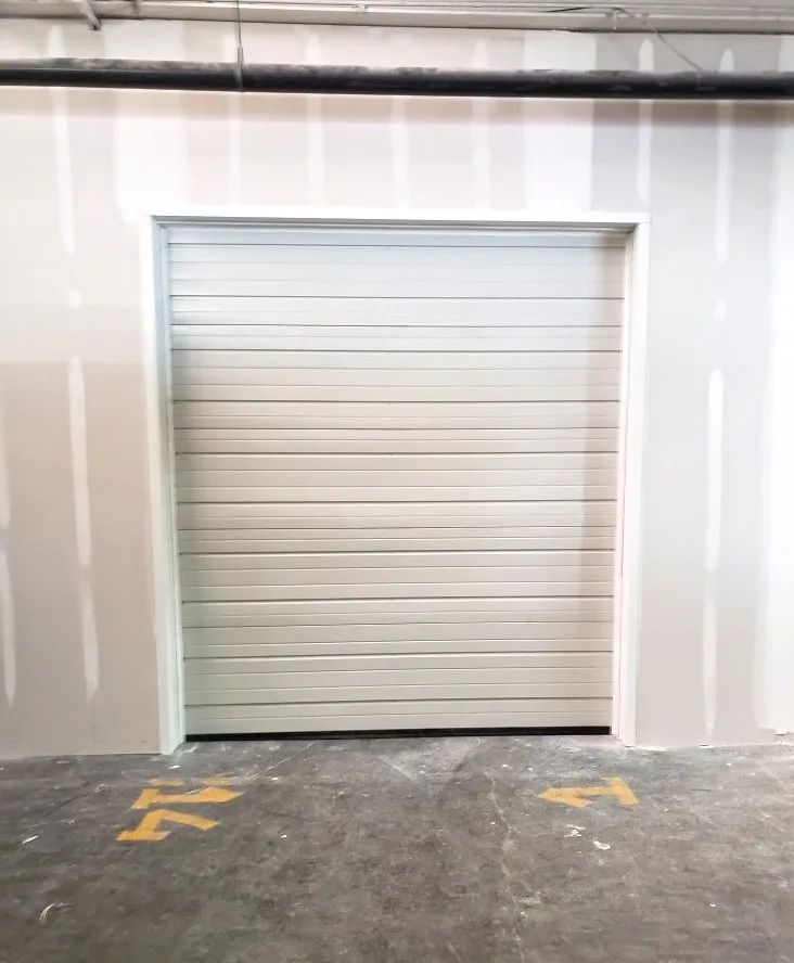 White roll-up garage door centered in a plain industrial wall with a concrete floor.