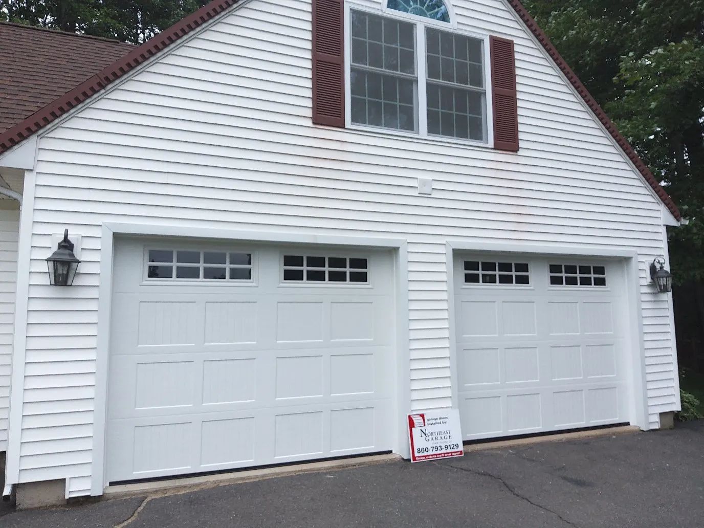 White two-car garage with a brown shingled roof and white siding at the end of a driveway