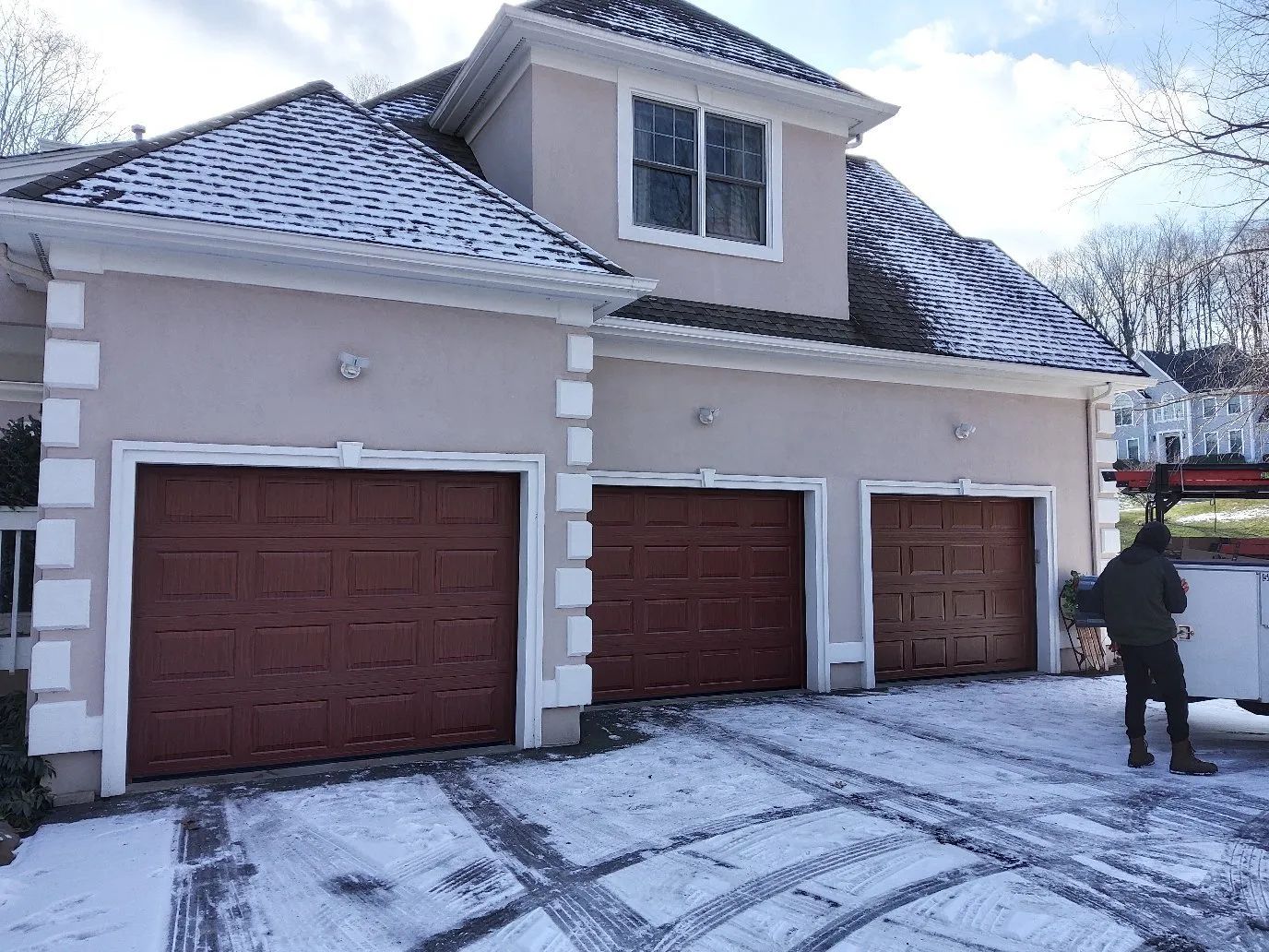 Snow-covered driveway and three-car garage with a person standing near the right side.