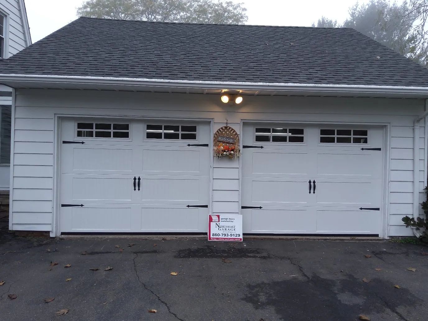 White double garage doors on a house with a sign hanging between them.