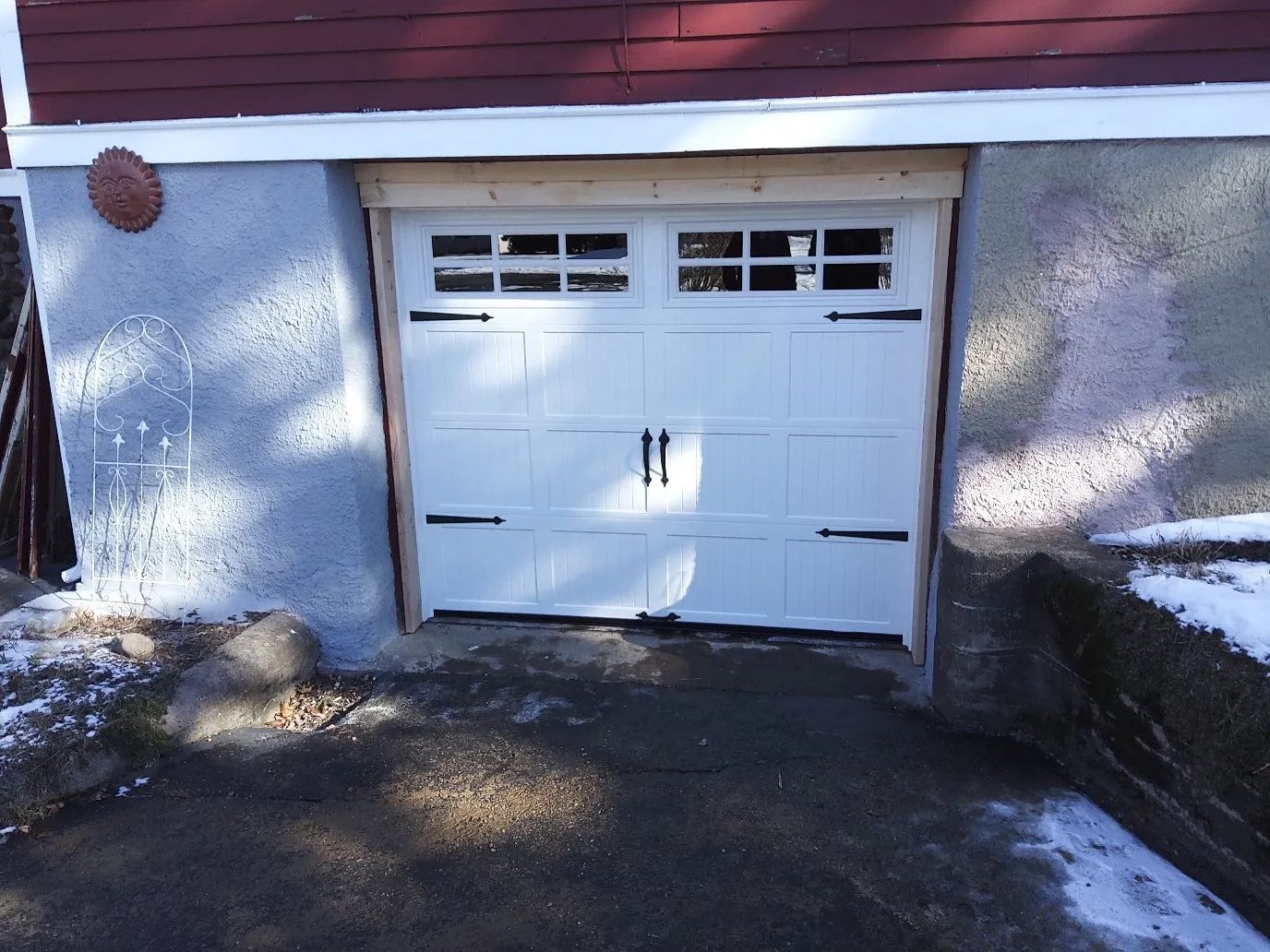 White garage door set into a light blue stucco wall beside a driveway in sunlight.