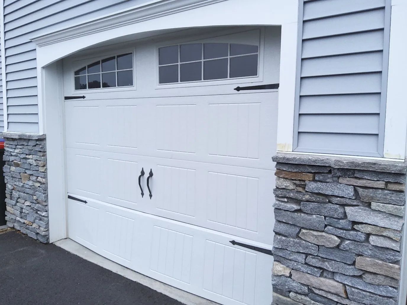 White double garage door with arched windows, set in a light gray house with stone accents.