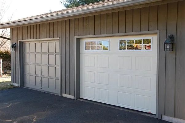 Two adjacent garage doors, one gray and one white, on a tan house exterior.