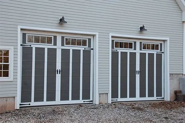 Two white-and-gray garage doors on a light gray house exterior, each with small windows above.