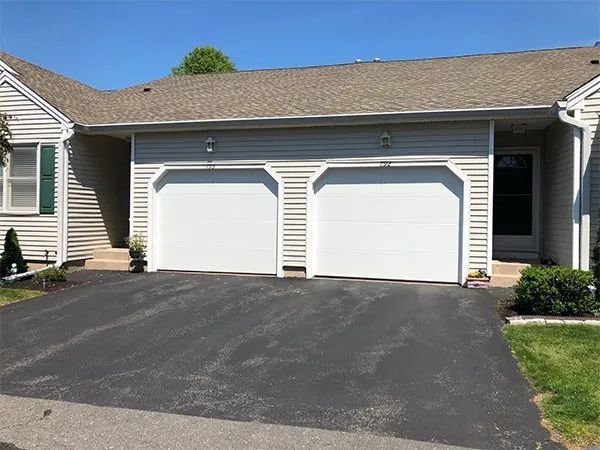 Suburban house exterior with two white garage doors and a dark asphalt driveway
