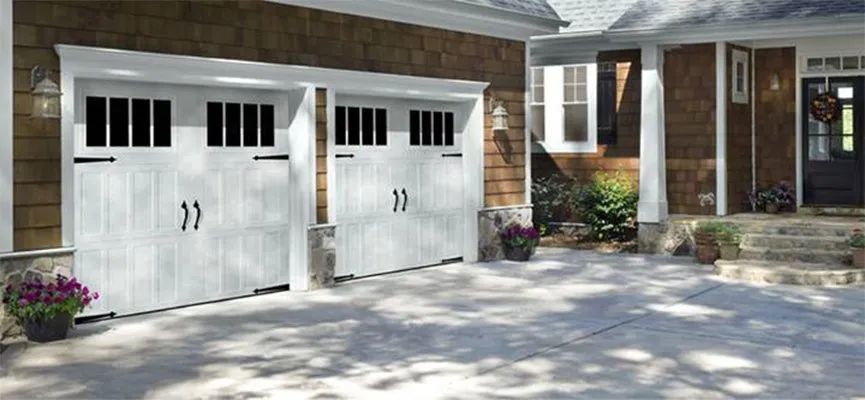 Two white garage doors on a brick house with a paved driveway and small flower beds