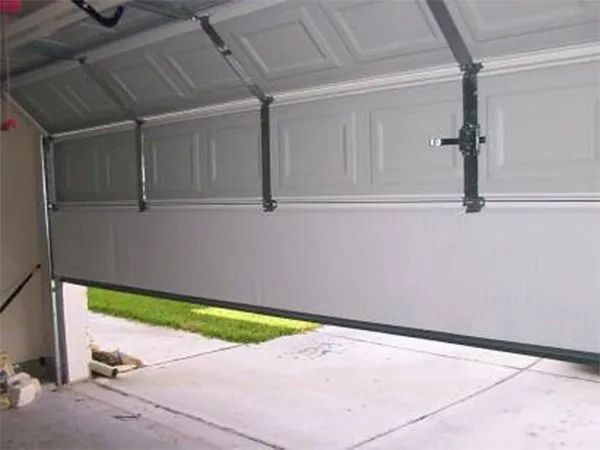 Garage door partially open, showing driveway and a strip of grass outside.