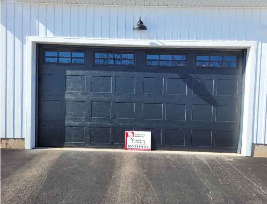 Black garage door on white building with a small sign at the base of the driveway