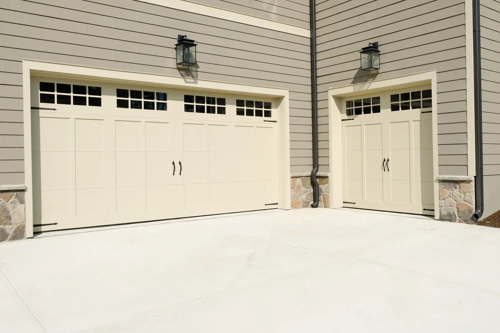 Two beige garage doors beside a side entry door on a snow-covered driveway