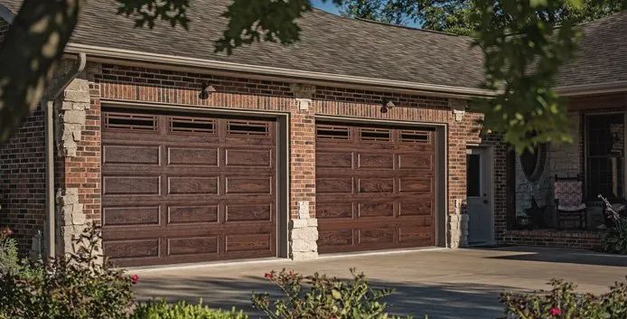 Two brown garage doors on a suburban house with a driveway and trees in front