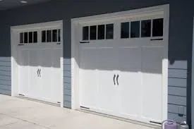 Two white garage doors with black window panes on a light blue house exterior