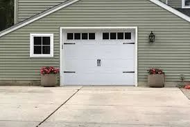 Suburban garage with white double door, small window, and two potted flower arrangements by the driveway.