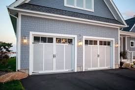 Two white garage doors on a gray house exterior with dark asphalt driveway and wall lanterns