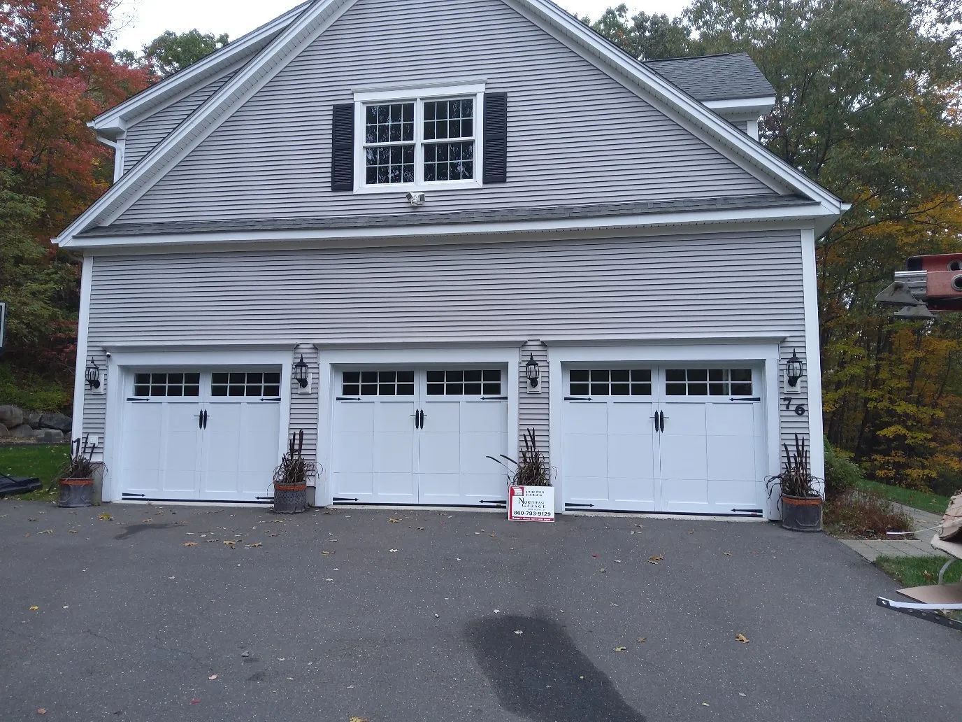 Three-car white garage with black shutters and a driveway in front of a gray house