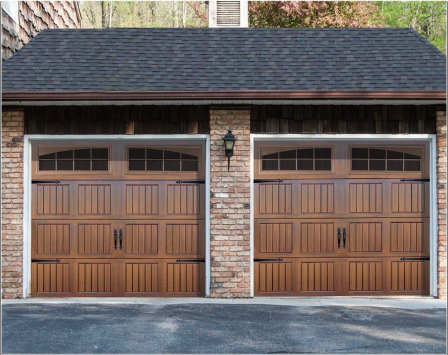 Two wooden garage doors with brick trim on a house exterior