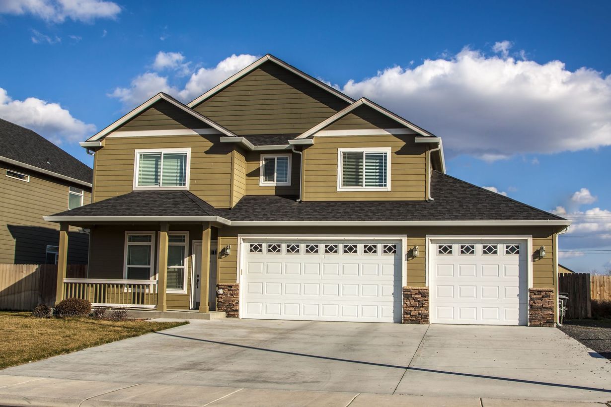 Two-story beige house with attached two-car garage and driveway under a partly cloudy sky