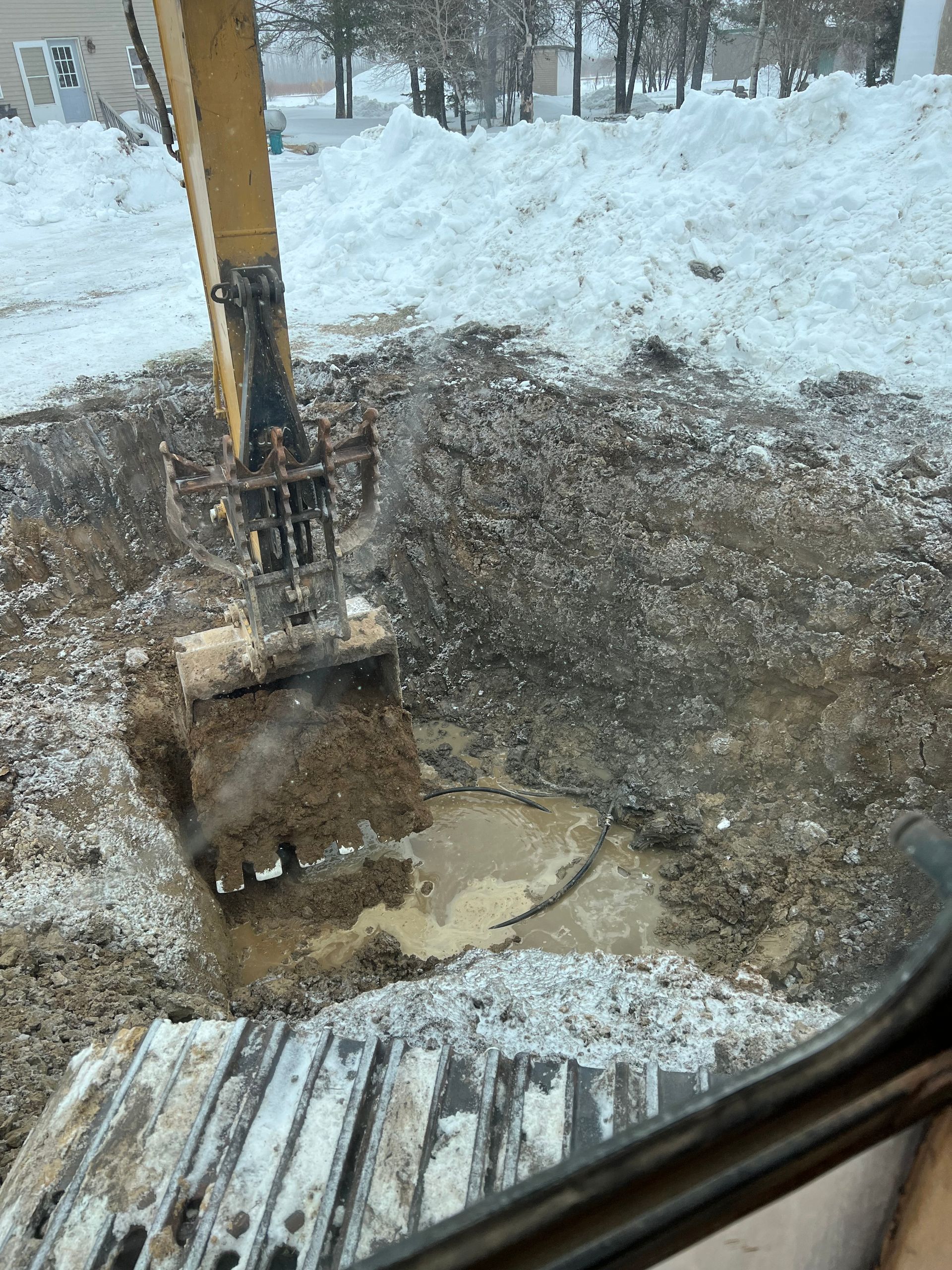 A large excavator is digging a hole in the snow.